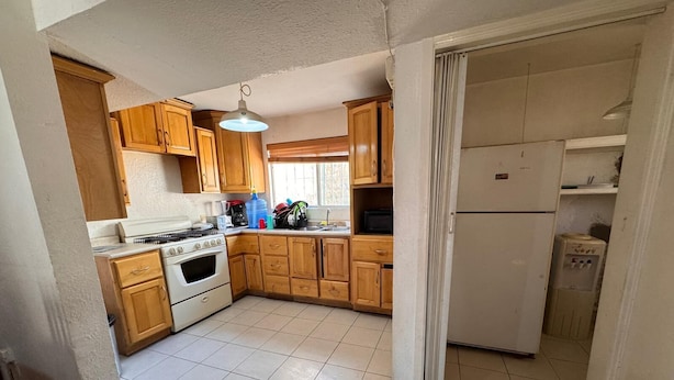 A kitchen with wooden cabinets, a stove, a refrigerator, and a water dispenser. - Consulado casa de Lujo (Ciudad Juárez)