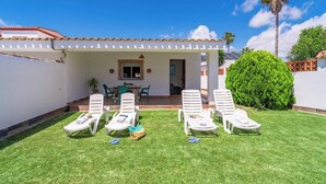 A patio with white lounge chairs and a small table, surrounded by a well-maintained lawn and a white building with a tiled roof. - Zona tranquila cerca de playa Conil de la Frontera by Ruralidays (Cádiz)