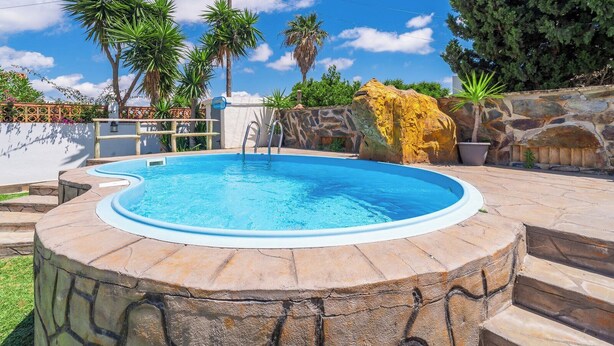 A circular swimming pool with a stone border, surrounded by a stone wall and various plants. - Zona tranquila cerca de playa Conil de la Frontera by Ruralidays (Cádiz)