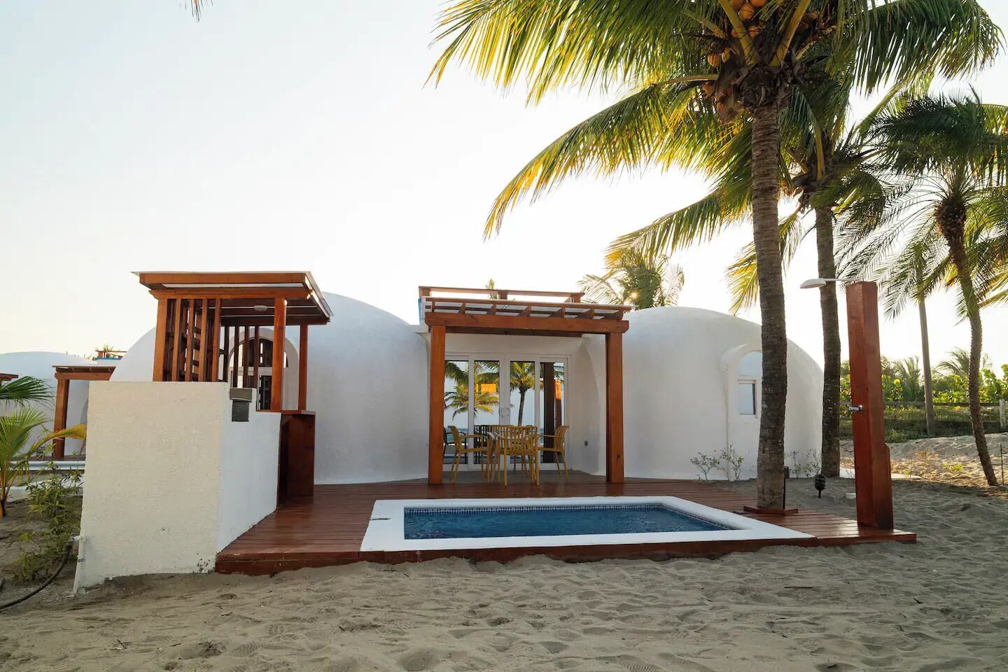 Una propiedad frente a la playa con piscina, pérgola de madera y palmeras.