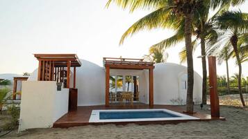 Una propiedad frente a la playa con piscina, pérgola de madera y palmeras.
