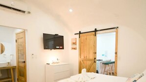 A hotel room with two beds, a TV mounted on the wall, a wooden door, and a small kitchenette visible through an open door.