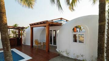 A poolside area with a wooden deck, a pergola, and a covered seating area with chairs.