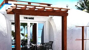 Una zona de piscina con una terraza de madera, una pérgola y un letrero que dice "TORNADE".