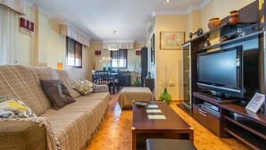 A living room with a sofa, a coffee table, a TV, and a dining area with a table and chairs.