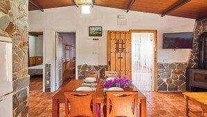 A dining area with a stone wall, wooden table, and chairs. There is a TV mounted on the wall and a fireplace. - El Mirador Jerez de la Frontera by Ruralidays (Cádiz)