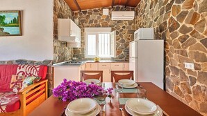 A compact kitchen with stone walls, a dining area with a table set for two, and a red sofa with a cushion. - El Mirador Jerez de la Frontera by Ruralidays (Cádiz)