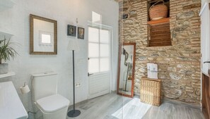 A bathroom with a toilet, a mirror, a lamp, and a stone wall. - Flamenco y Sol Lecrín by Ruralidays (Granada)