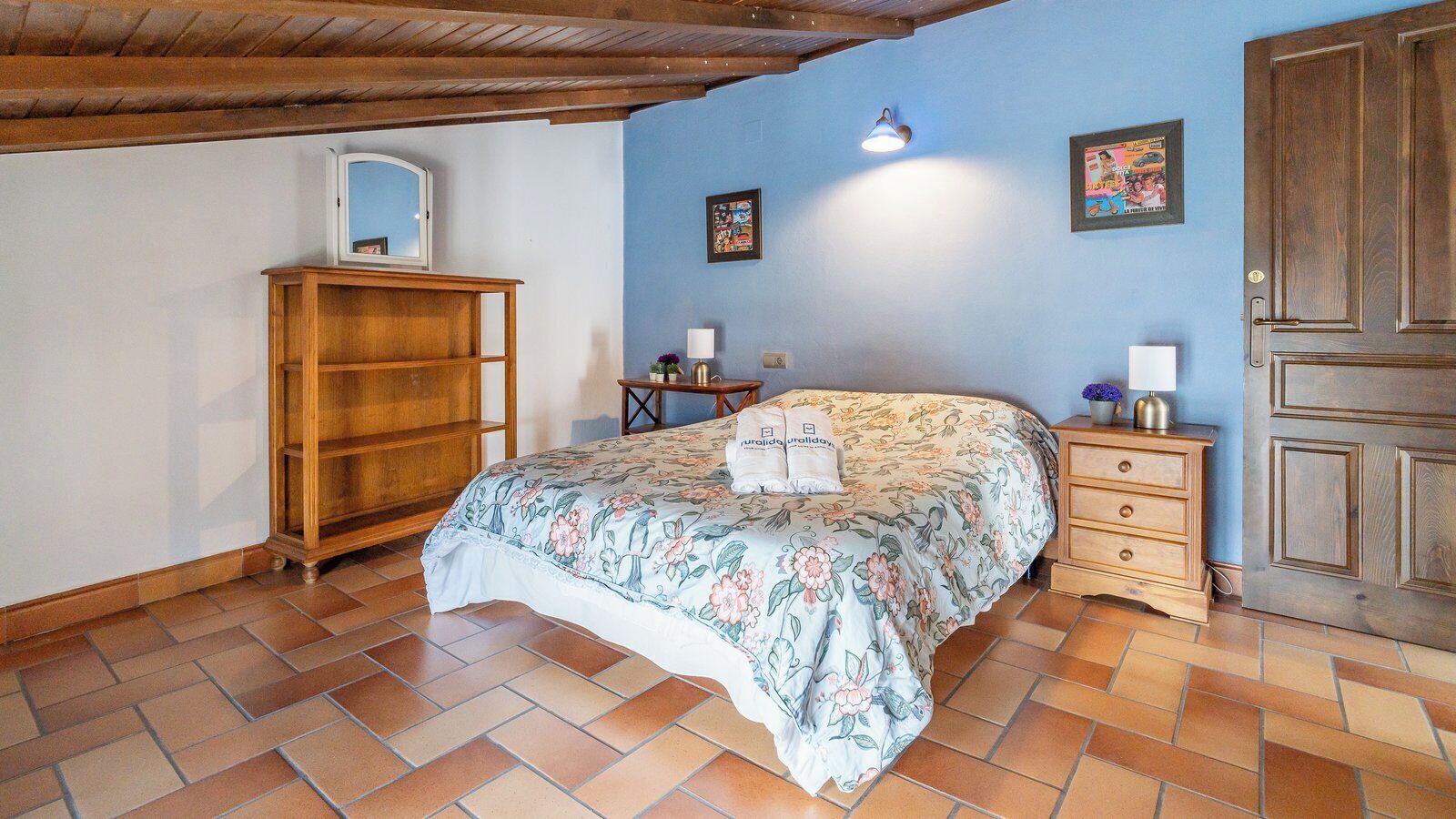 Een slaapkamer met een bed, een houten garderobe, nachtkastje en een deur.