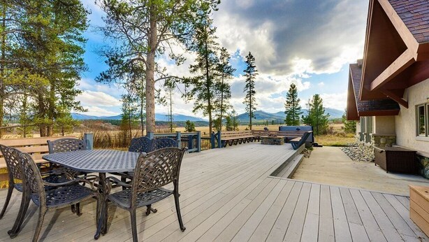 An outdoor patio with a round table and chairs, surrounded by a wooden deck and a stone wall. - Beautiful 4-bedroom house on 8 acres near Fraser - privacy and amazing views!
 (Fraser)