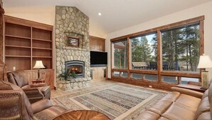 A cozy living room with a stone fireplace, leather sofas, wooden shelves, and large windows offering a view of the outdoors. - Beautiful 4-bedroom house on 8 acres near Fraser - privacy and amazing views!
 (Fraser)