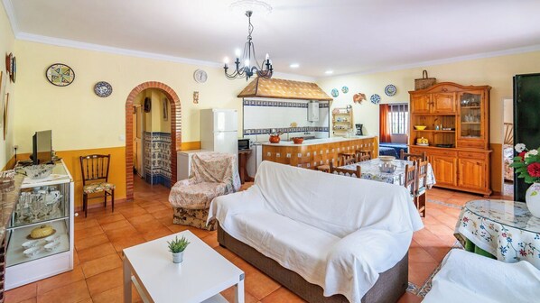 A cozy living room with a sofa, chairs, a dining table, and a kitchen area with a tiled backsplash.