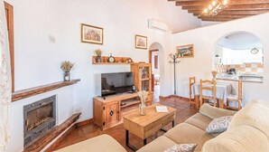 A cozy living room with a fireplace, wooden furniture, a television, and a dining area with a kitchen visible in the background. - Casa El Limonero Cómpeta by Ruralidays (Málaga)