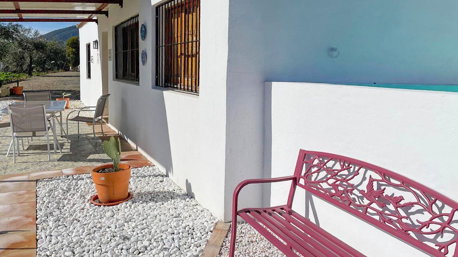 Une terrasse avec un mur blanc, un banc rouge et une plante en pot.
