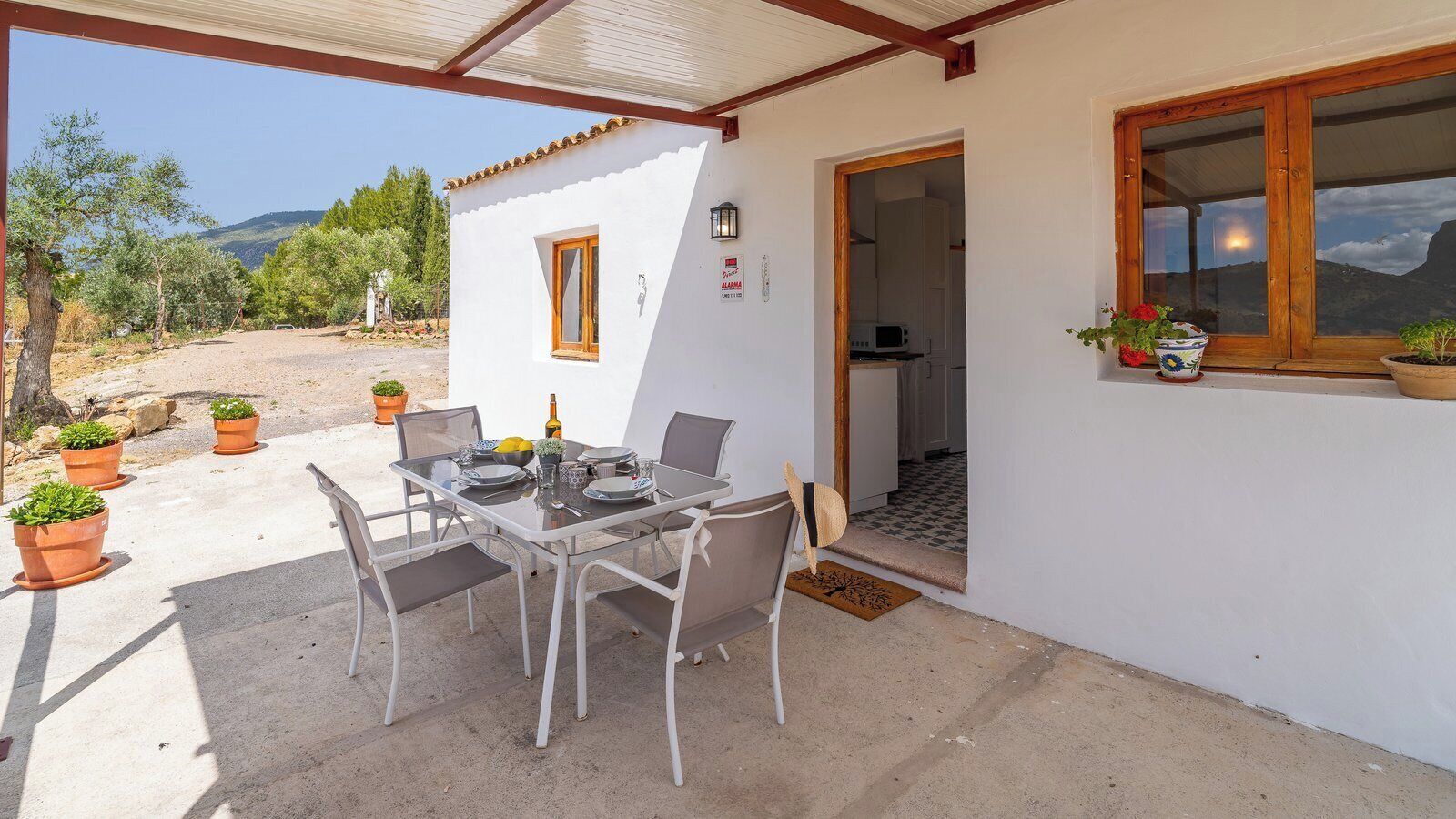 Un espace extérieur abrité, aménagé pour les repas, avec une table et des chaises, des plantes en pot et une vue sur le paysage environnant.