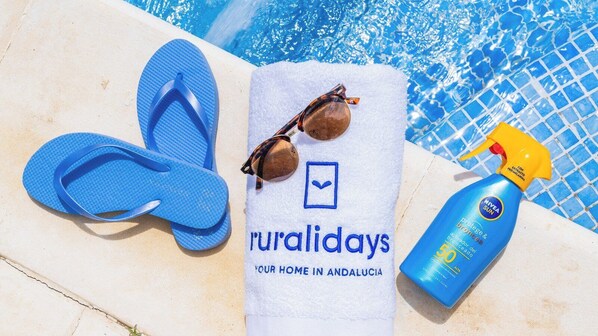 Een handdoek met de tekst 'ruralidays JE THUIS IN ANDALUSIË' en een fles zonnebrandcrème.