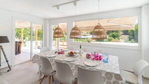 A dining area with a table set for four, surrounded by white chairs, with a view of greenery outside. - Villa Higuera Nerja by Ruralidays (Málaga)