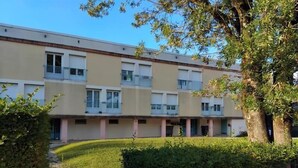 A multi-story building with balconies, a paved pathway, and a well-maintained hedge.
