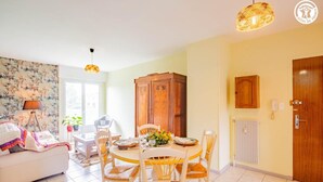 A cozy living room with a dining area, featuring a round table, wicker chairs, and a wooden cabinet.