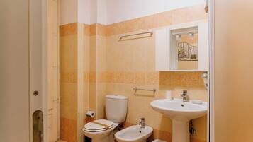 A bathroom with a toilet, bidet, sink, and a towel rack.