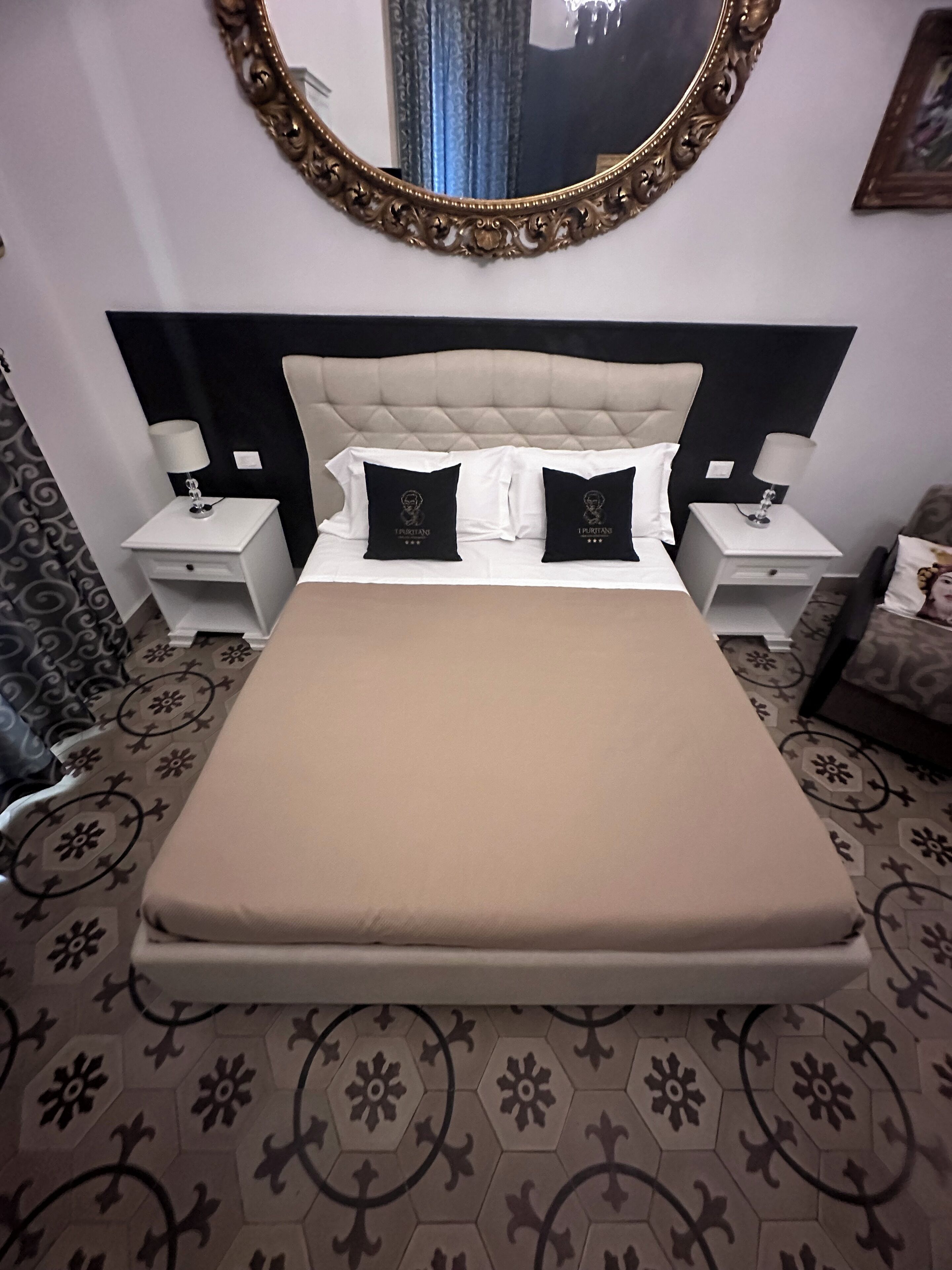 A bedroom with a large bed, two nightstands, a decorative mirror, and patterned carpet.