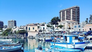 A marina with boats docked, surrounded by buildings and clear blue water. - B&B I Puritani (Catania)