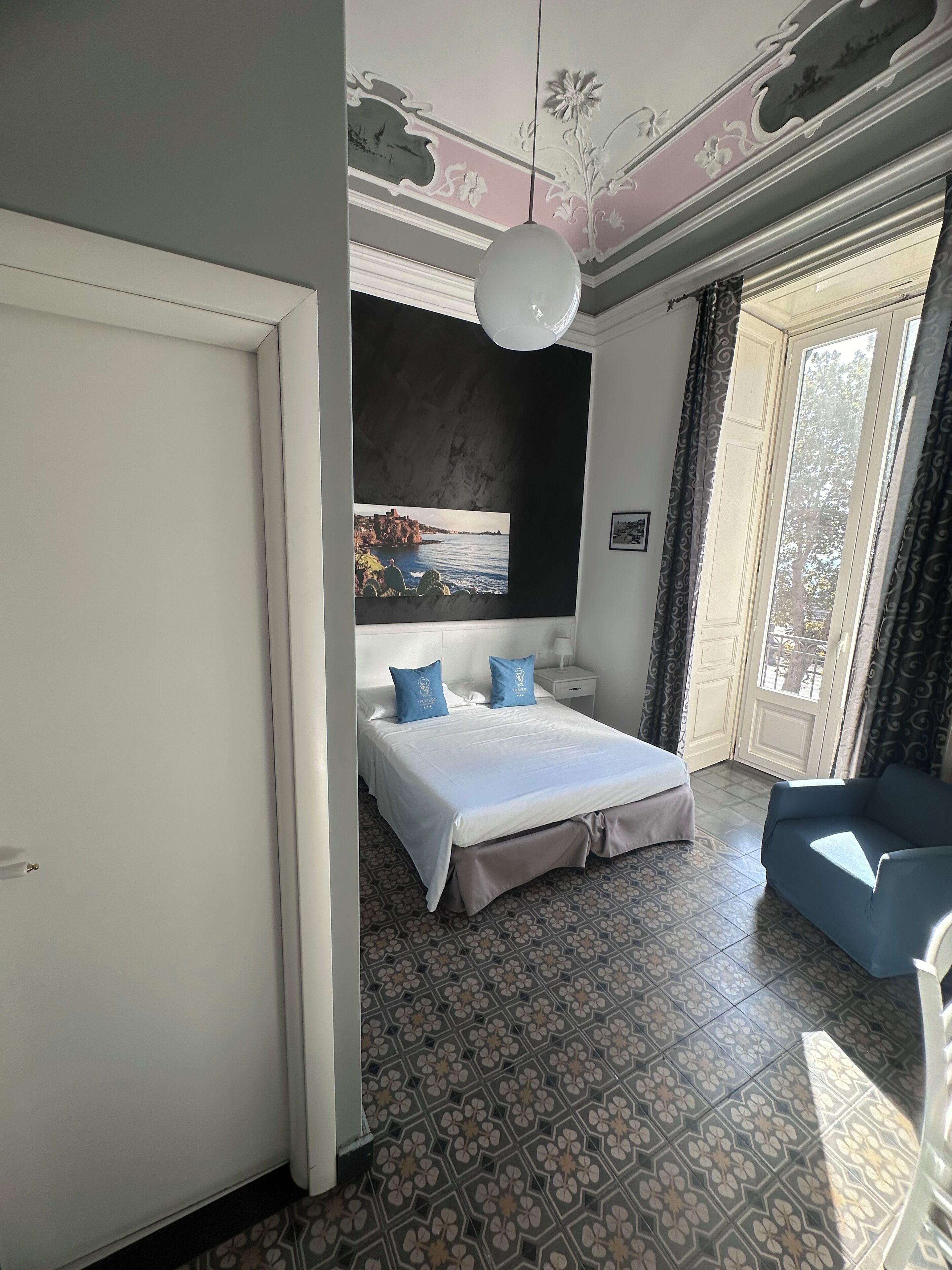 A bedroom with a bed, a sofa, a painting, and patterned flooring.