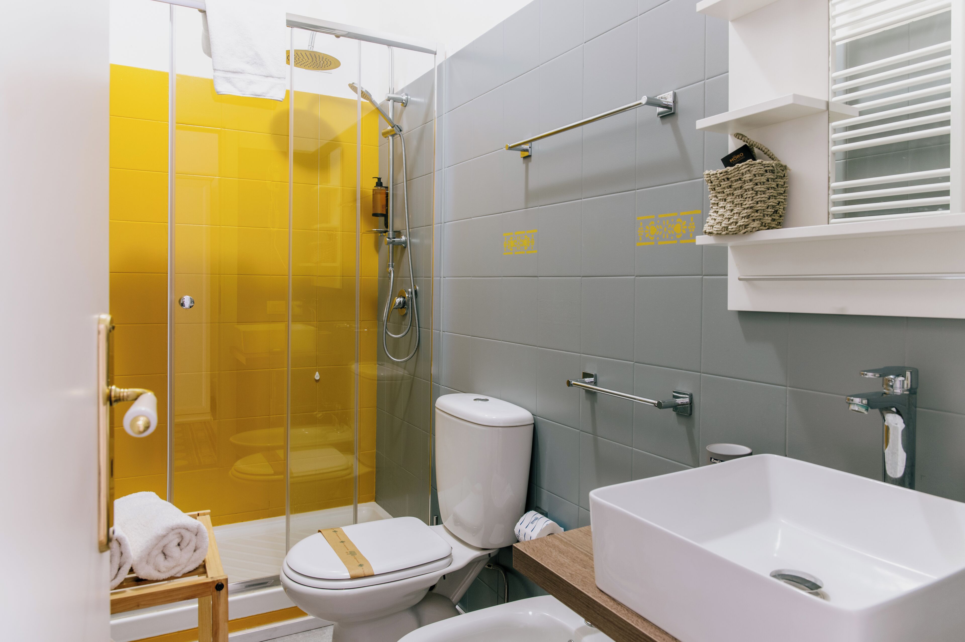A modern bathroom with a glass shower enclosure, a white toilet, a large bathtub, and a wooden shelf with toiletries.