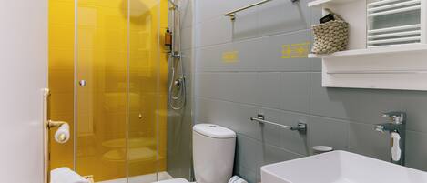 A modern bathroom with a glass shower enclosure, a white toilet, a large bathtub, and a wooden shelf with toiletries.