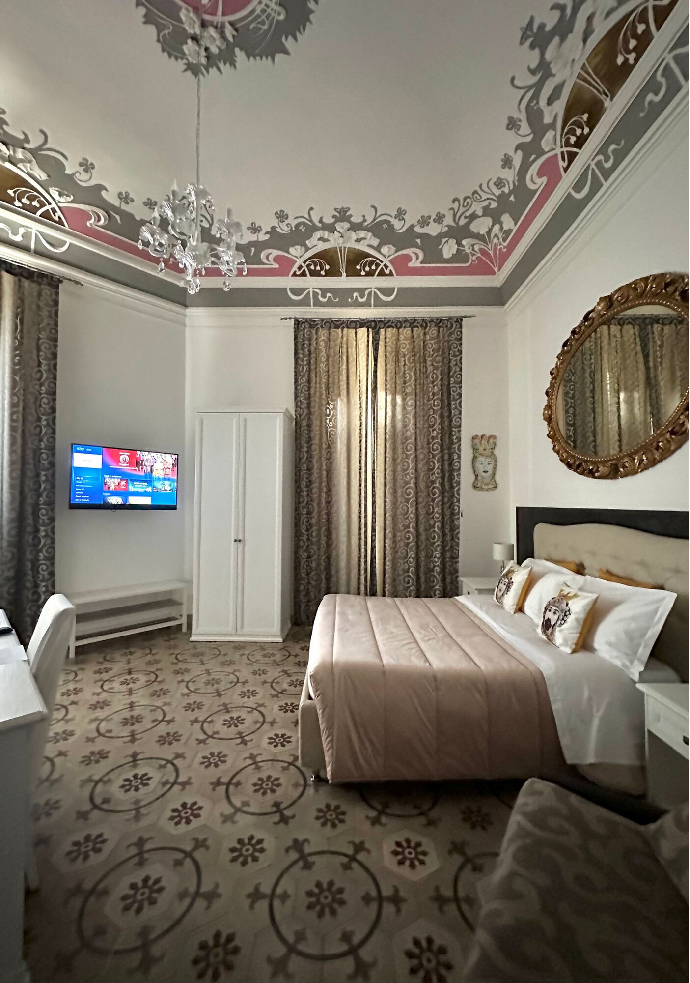 A bedroom with a bed, a TV mounted on the wall, a wardrobe, and a mirror.