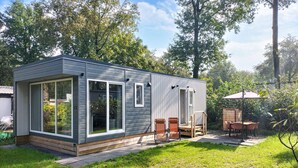 A modern, single-story cabin with large windows, a patio with outdoor furniture, and a surrounding wooded area. - Pet friendly home in Mariënberg (Mariënberg)