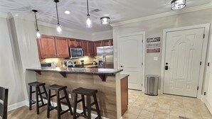 A modern kitchen with wooden cabinets, a stainless steel refrigerator, and a bar area with stools.