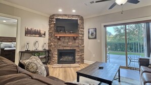 A living room with a stone fireplace, a ceiling fan, and a large TV mounted on the wall.
