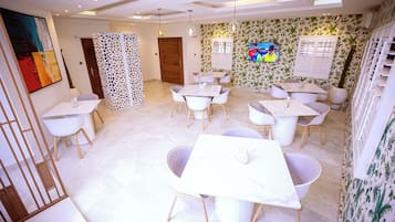 Un comedor moderno con mesas y sillas blancas, una pantalla decorativa y un televisor en la pared.