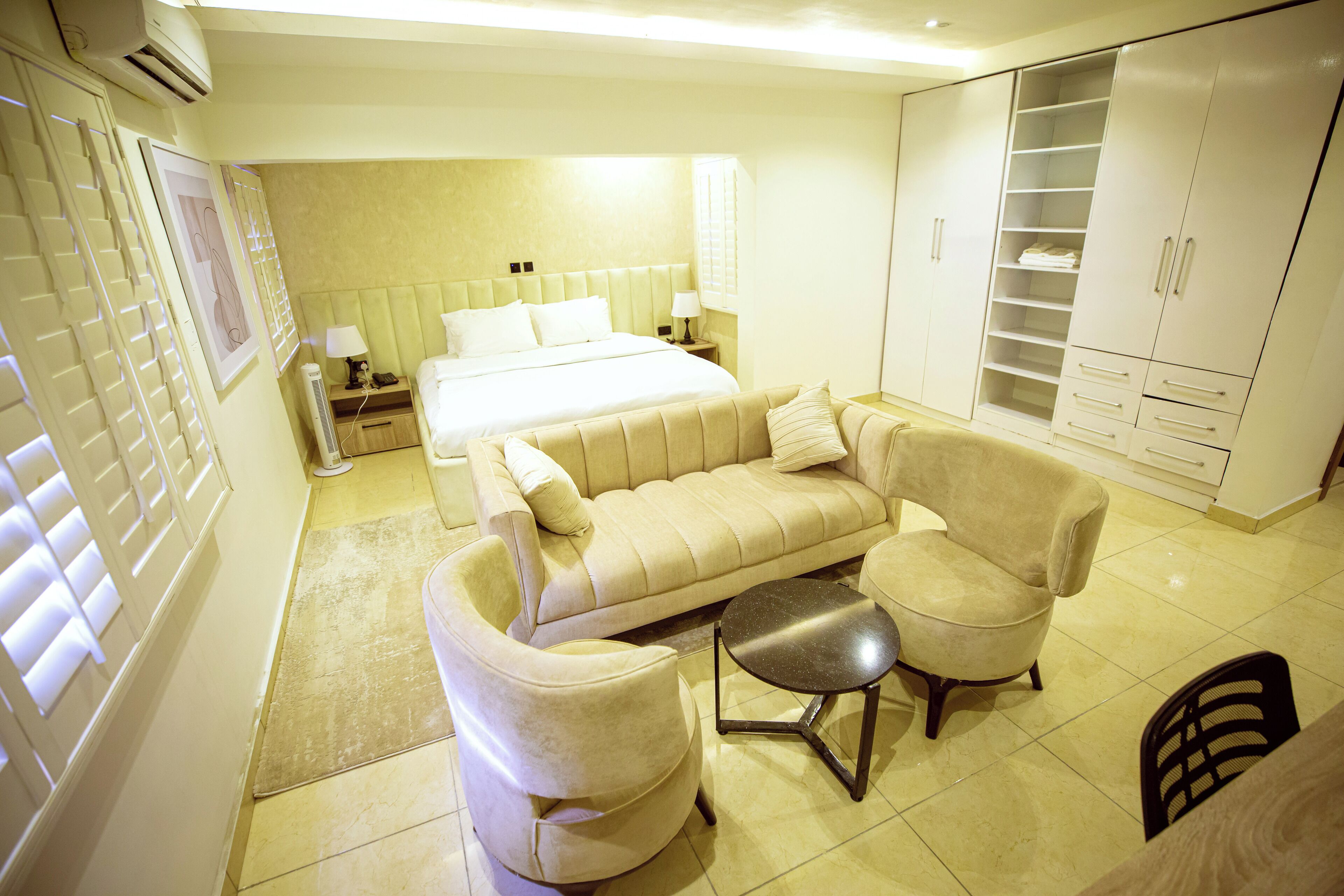 A bedroom with a bed, a sofa, a chair, a small table, and a wardrobe.