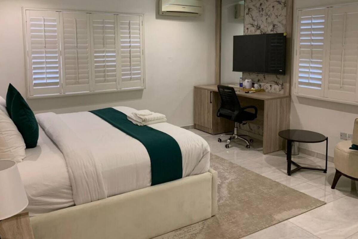 Une chambre à coucher comprenant un lit, une table de chevet, une lampe, un bureau, une chaise et un téléviseur.