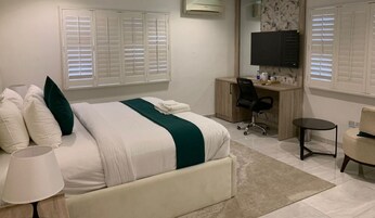 A bedroom with a bed, bedside table, lamp, desk, chair, and TV.