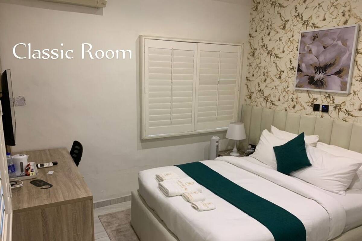 Une chambre classique, avec un lit, une table de chevet et une fenêtre avec des volets.