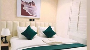 Une chambre à coucher bien rangée, avec un grand lit, une table de chevet avec une lampe et un tableau encadré au mur.