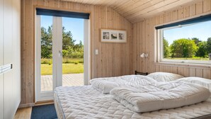 A bedroom with a bed, a door leading to an outdoor area, and a window with a view of greenery.