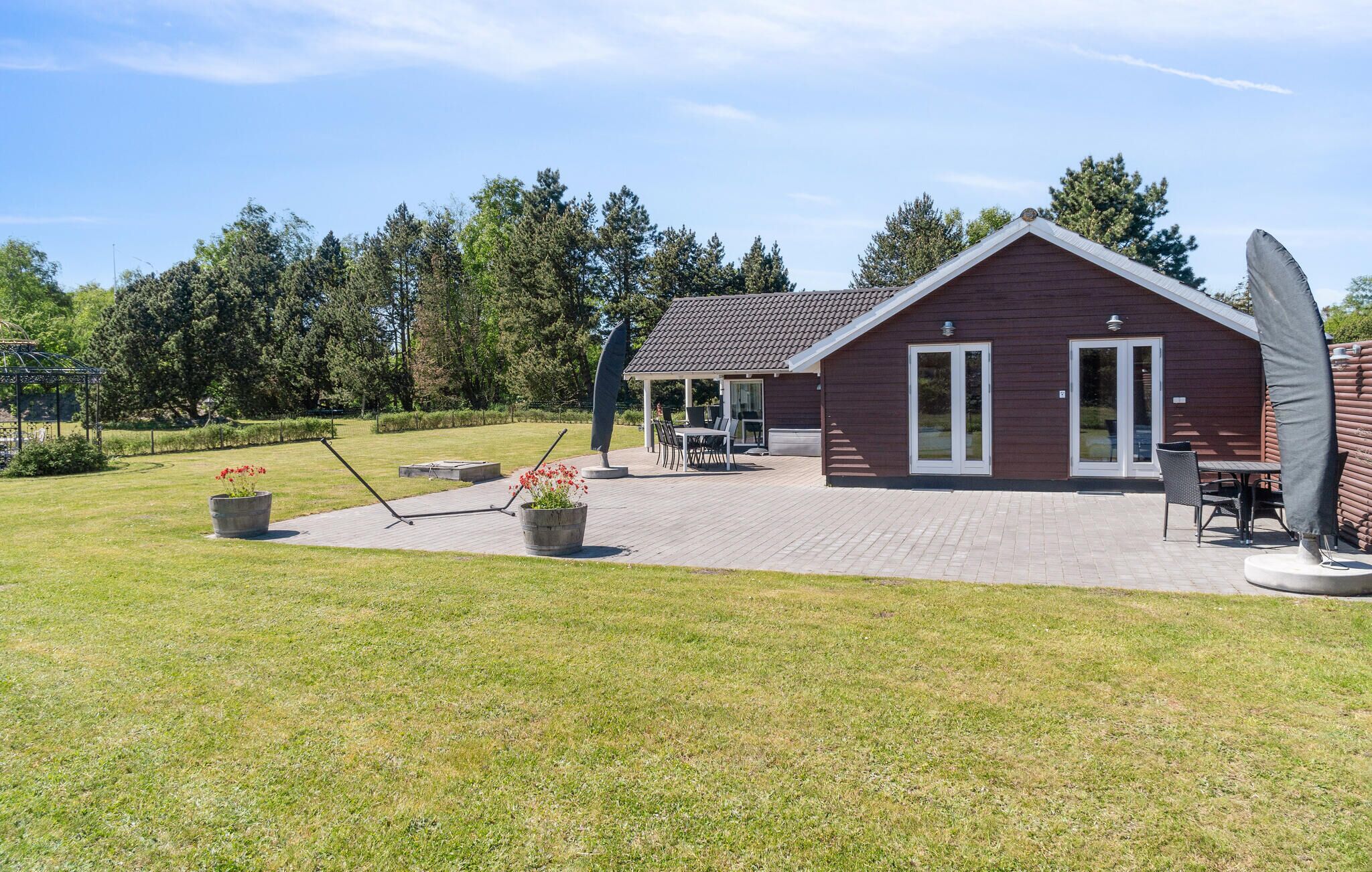 Ein modernes Haus mit Terrasse, überdachter Außenlounge und Garten mit Rasen und Bäumen.