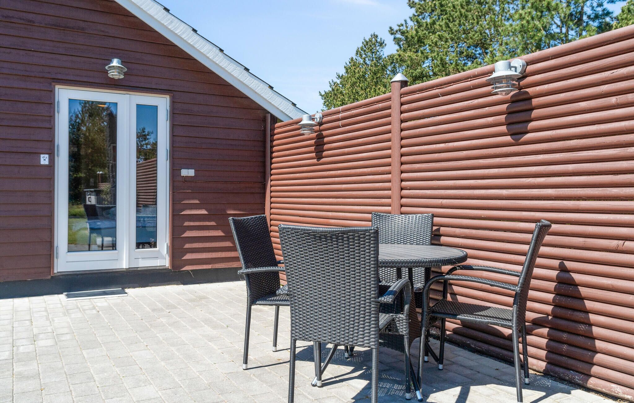 Patio esterno con mobili in vimini e recinzione in legno.