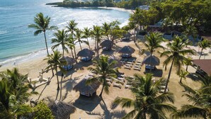 An aerial view of a beach with thatched-roof huts, sun loungers, and palm trees. - Beach Dreams (Puerto Plata)