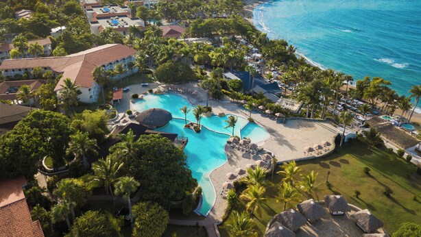 An aerial view of a resort with a large swimming pool surrounded by palm trees and a beach. - Beach Dreams (Puerto Plata)
