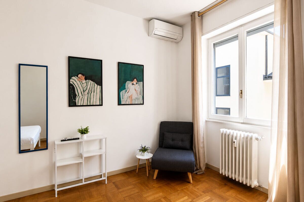 A room with a bed, a white console table, a black armchair, and two framed artworks on the wall.