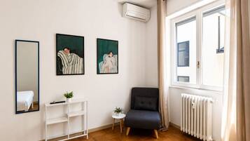 Ein Zimmer mit einem Bett, einem weißen Konsolentisch, einem schwarzen Sessel und zwei gerahmten Kunstwerken an der Wand.