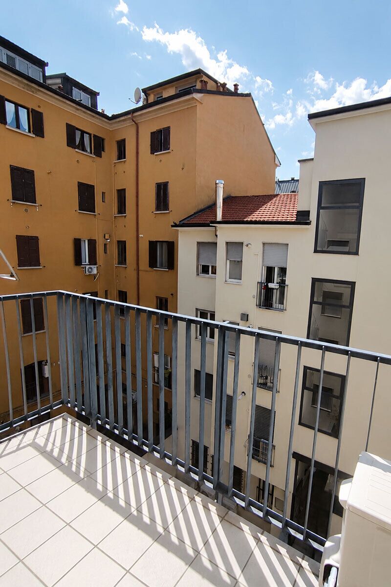 Un immeuble résidentiel à plusieurs étages, doté de balcons, d’un sol carrelé et surplombant un ciel dégagé.