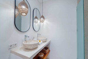 A bathroom with two round stone sinks, a mirror, and two hanging woven light fixtures. - Villa Camille (Tabanan)