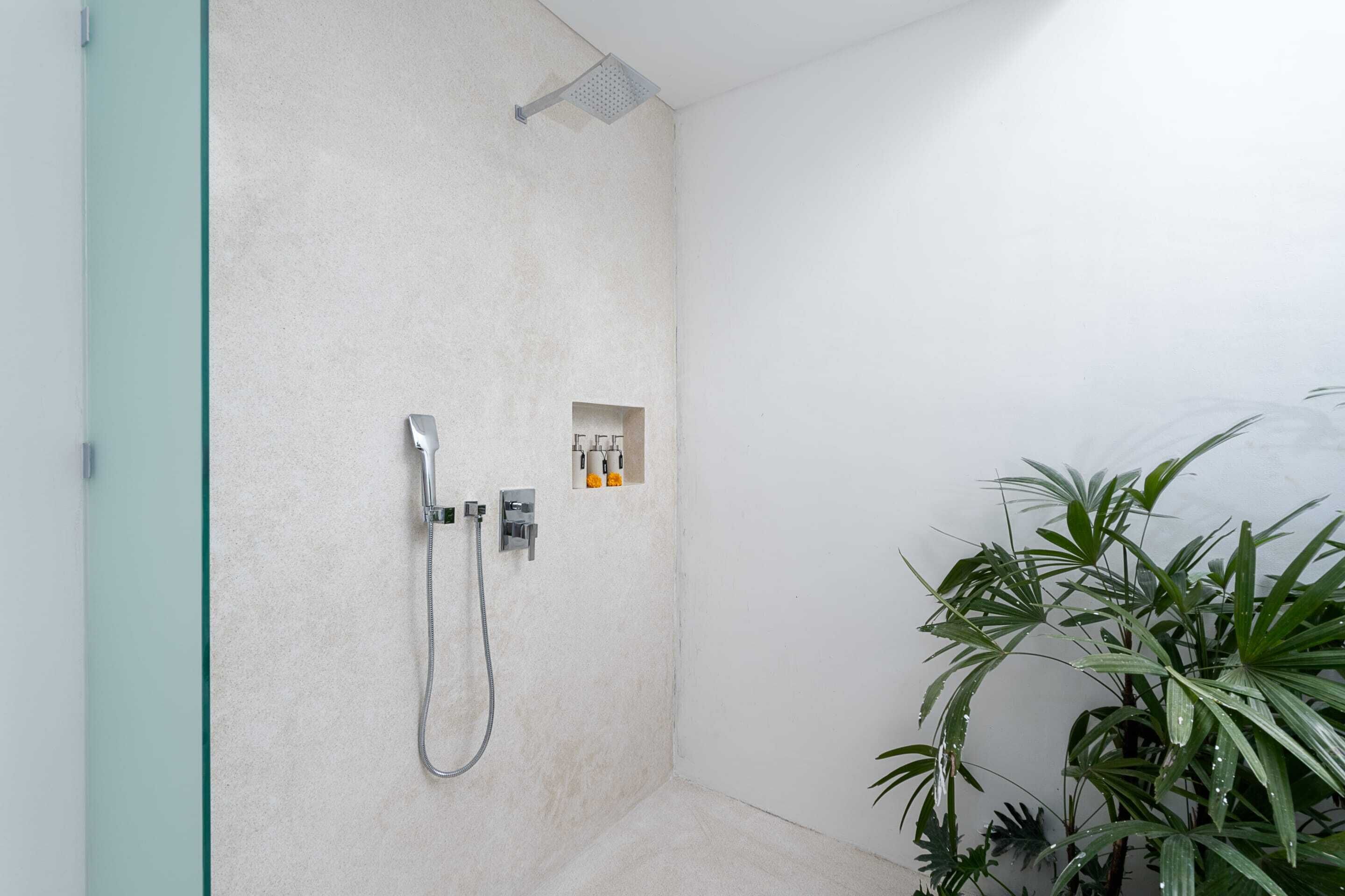 A shower area with a handheld showerhead and a wall-mounted control panel.