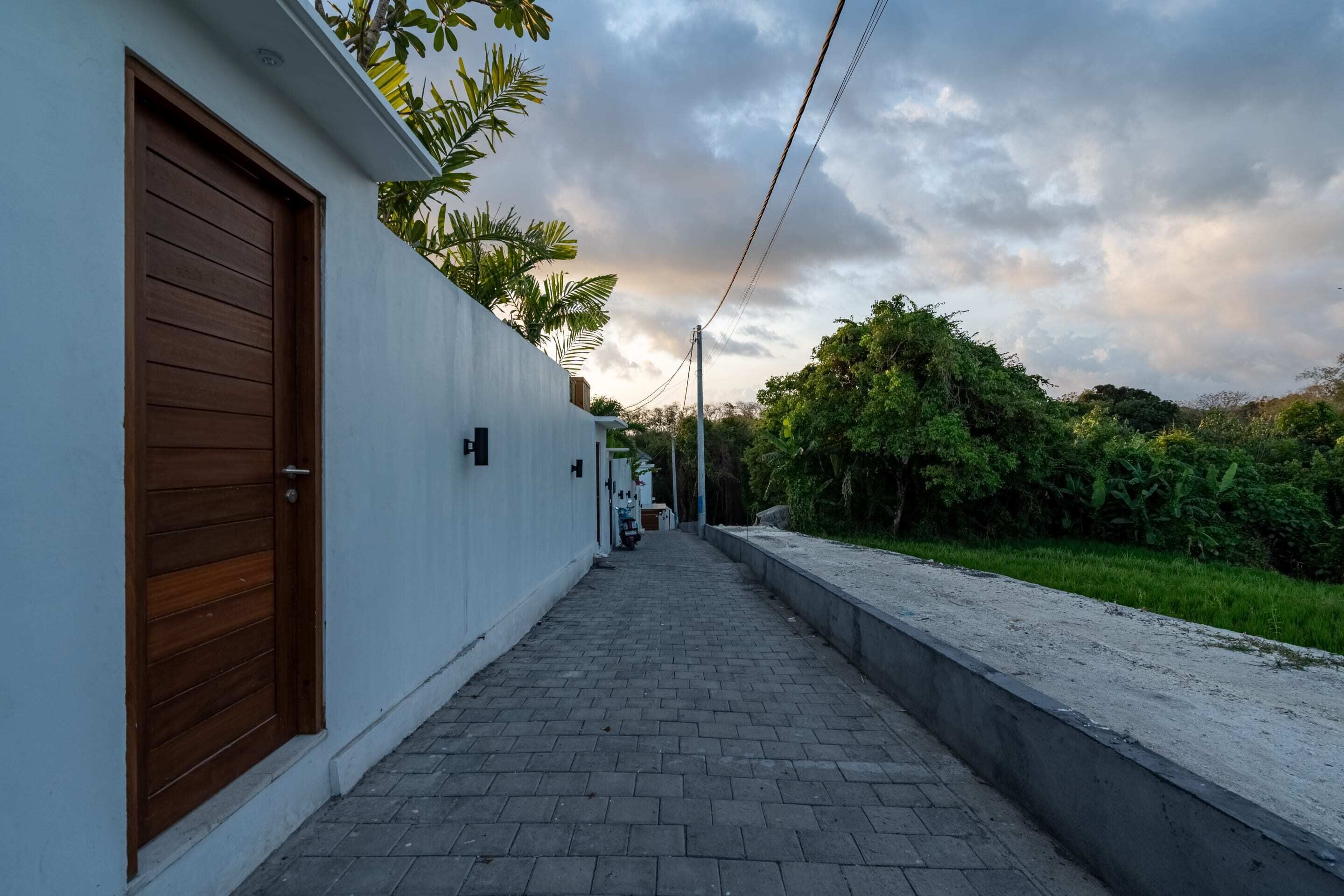 A narrow pathway leading to a building with a wooden door and a white exterior wall.